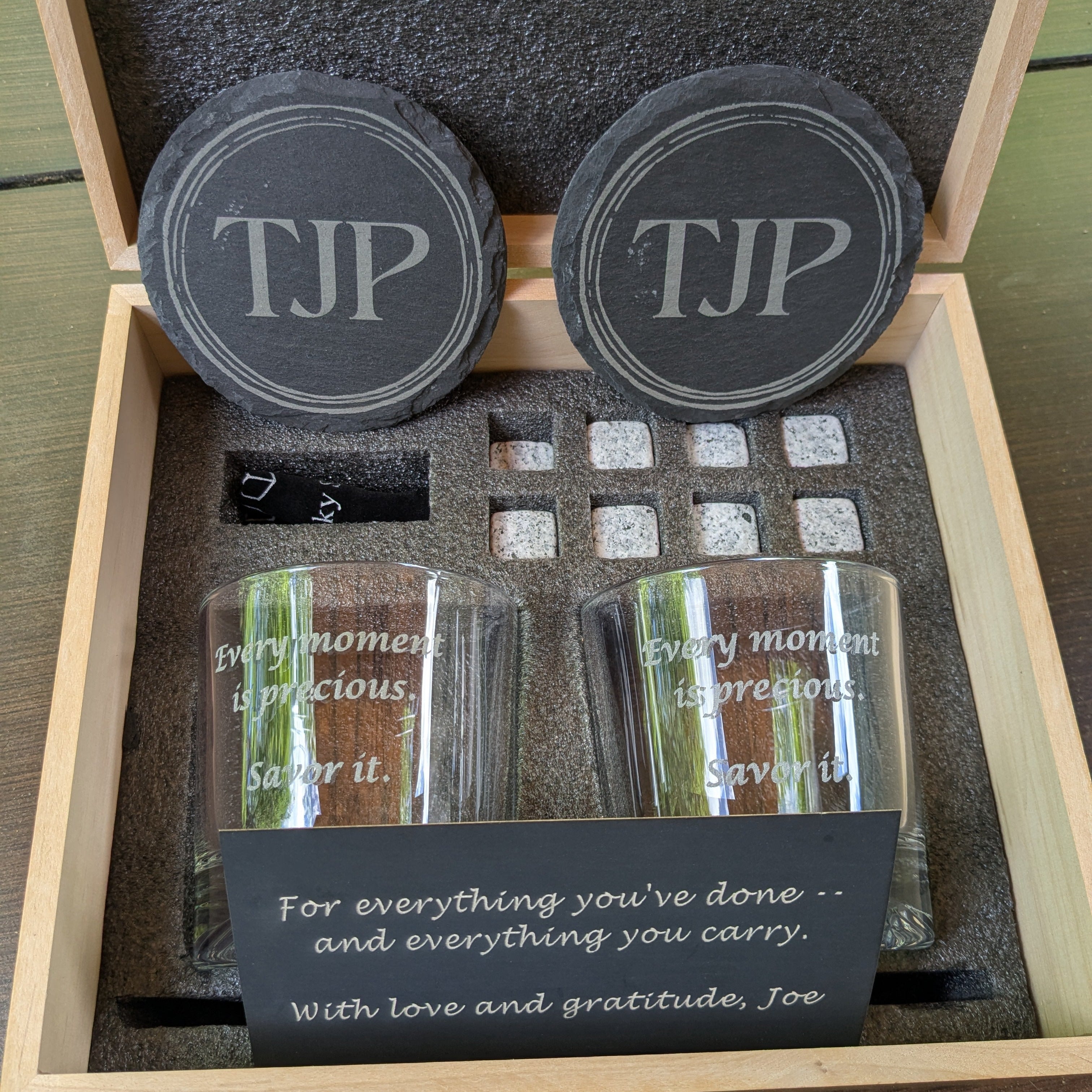 Two glass tumblers with engraved text in a wooden box, featuring 'TJP' on the lids.